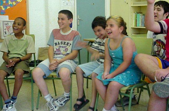 Middle school students sit in chairs in a semicircle, smiling.