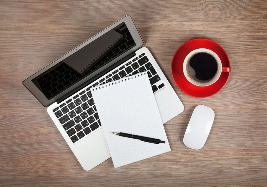 laptop, coffee, and pen and paper on a desk.