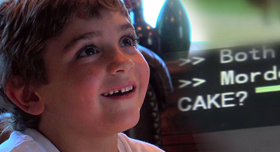 a young boy smiles as he looks up at a tv on the wall, playing a program with captions.