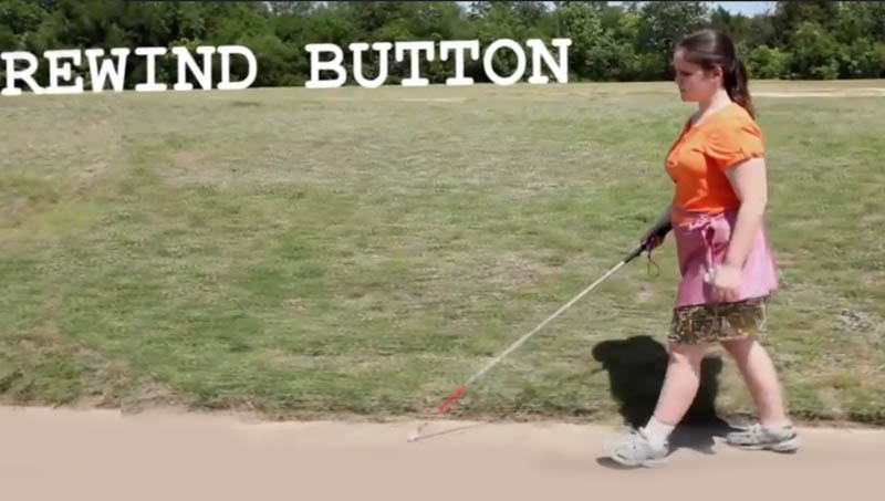 A girl with a white cane walks down a sidewalk.