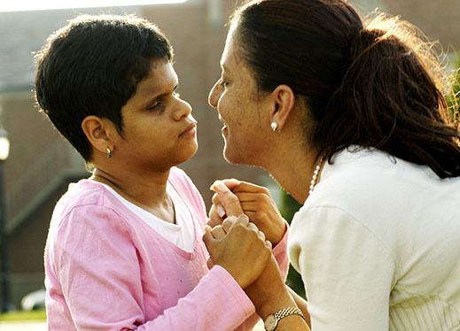 A young boy and his mother face each other, holding hands.