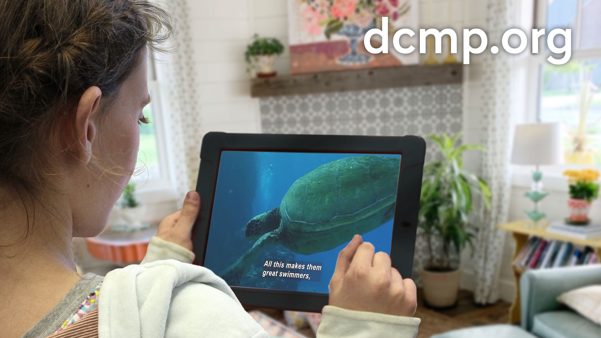 A young girl sits in her living room watching a captioned video on a computer tablet.