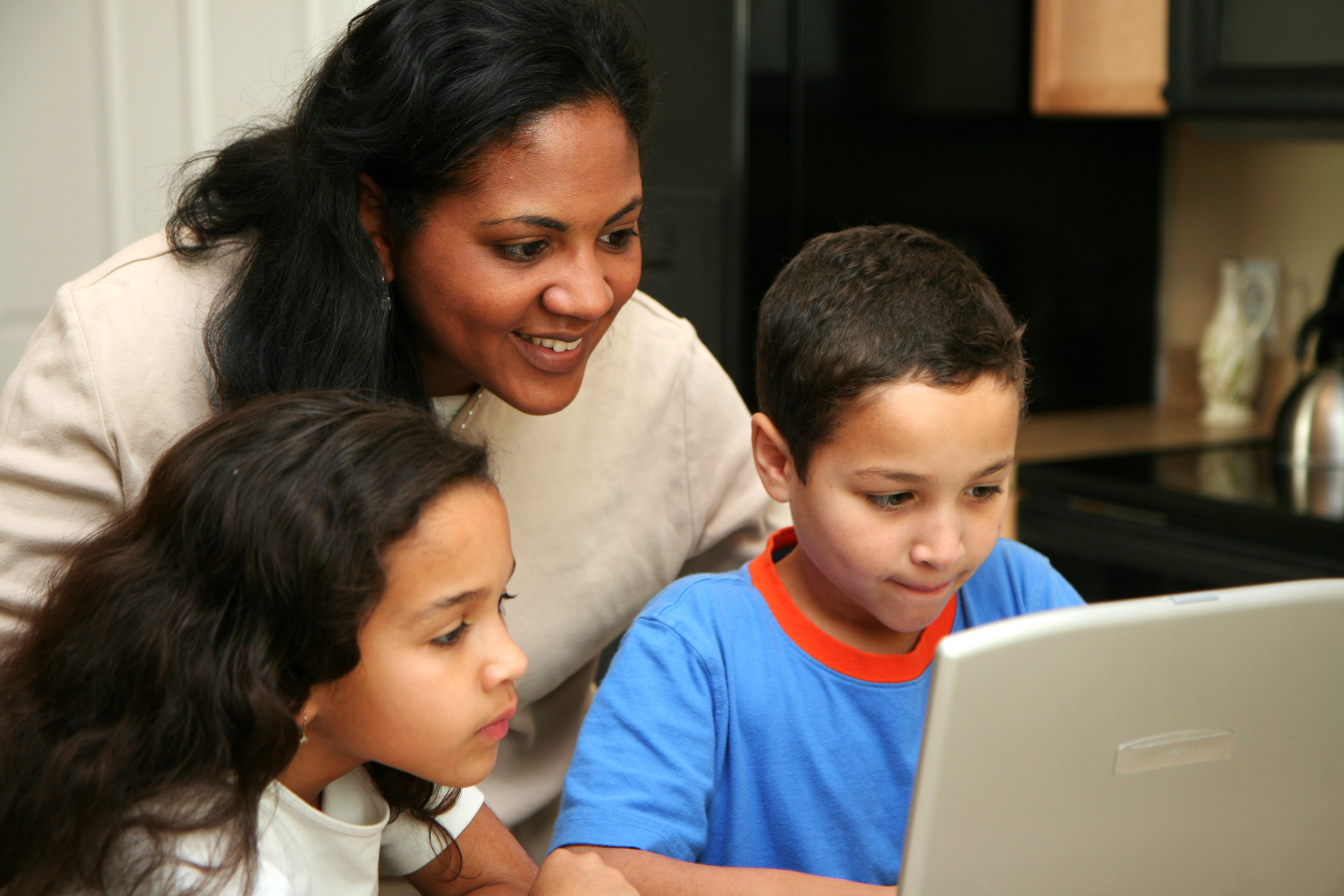 A mother and two children at home smiling and looking at a laptop screen.