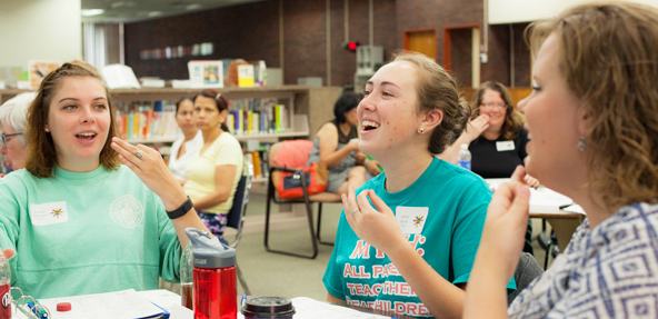 Teen girls communicate with cued speech hand and mouth movements.